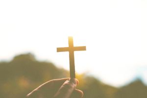 Close-Up Of Hand Holding Cross Against Sky