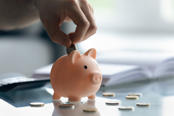 Close up male hand putting coins inside small piggybank.