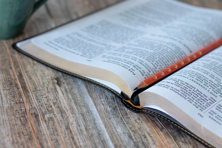 Open holy bible book with pencil and cup of coffee on wooden background