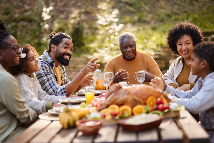 Happy African American extended family talking during Thanksgiving meal at picnic table.